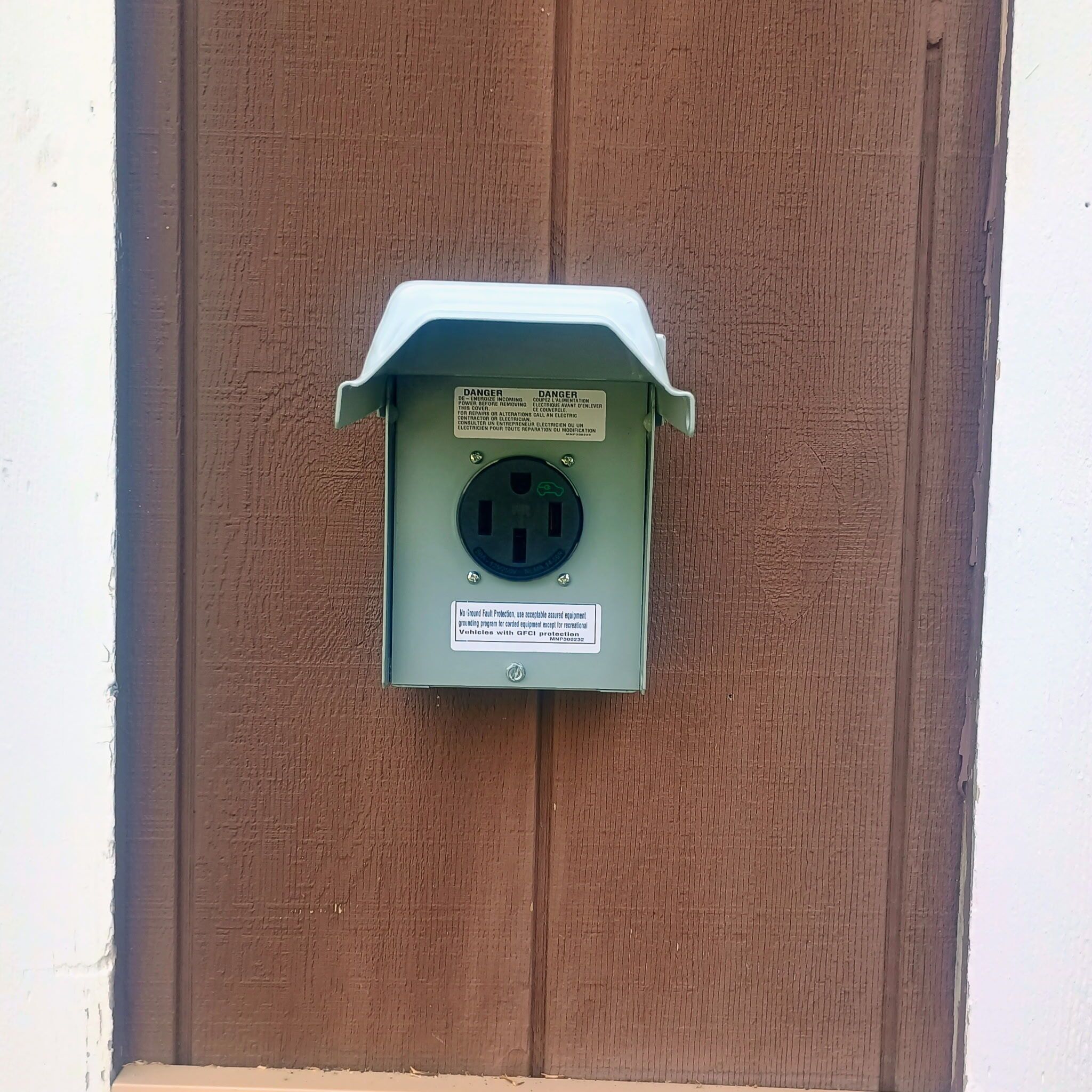 A utility meter box mounted on a brown wall with a warning label and a grounding protection sticker.