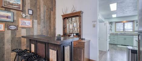 A kitchen with a wooden bar area, bar stools, and framed pictures on the wall.