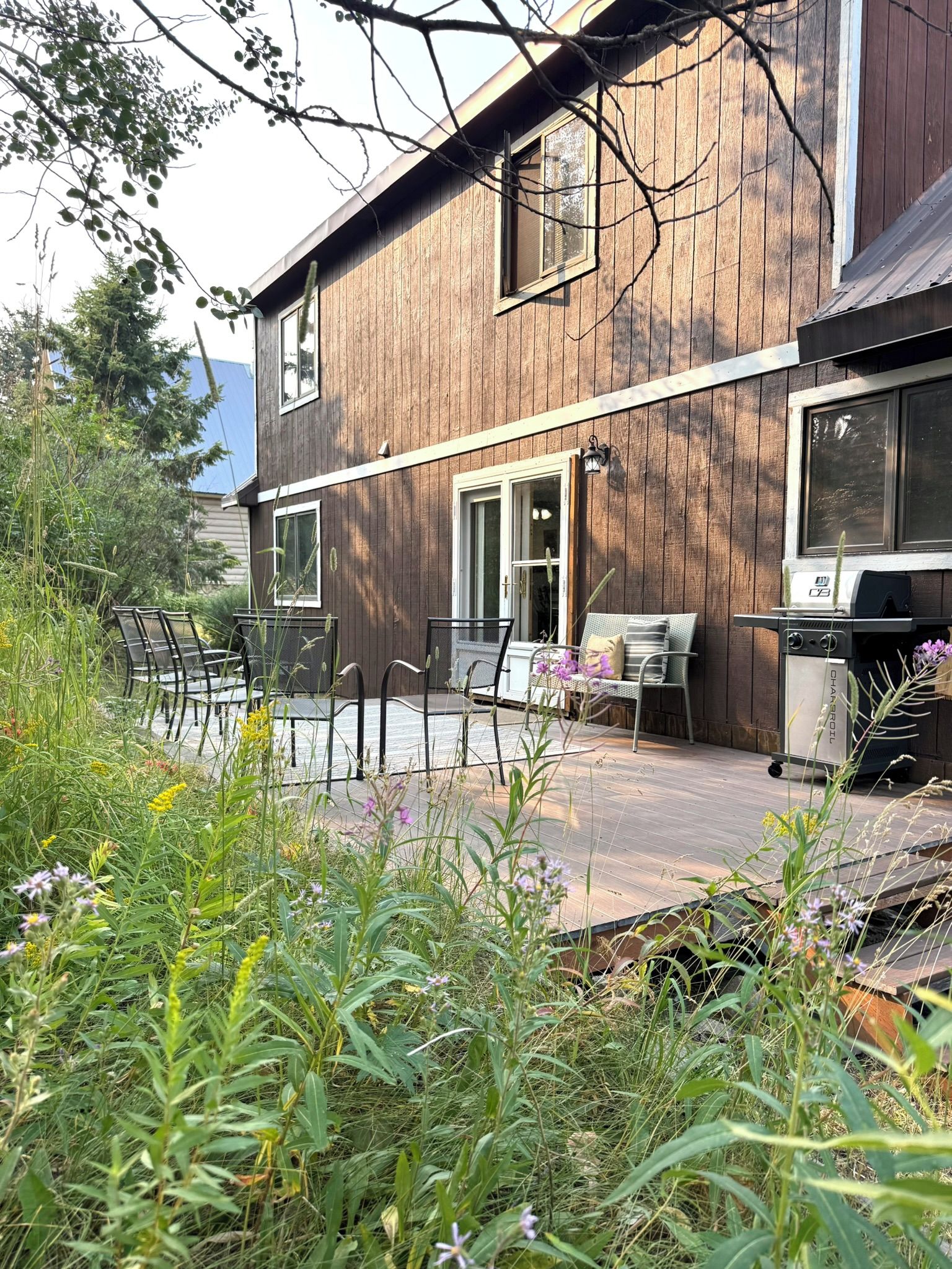 Una casa de madera con patio, mobiliario exterior y una parrilla.