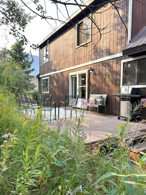 A wooden house with a patio, outdoor seating, and a grill.