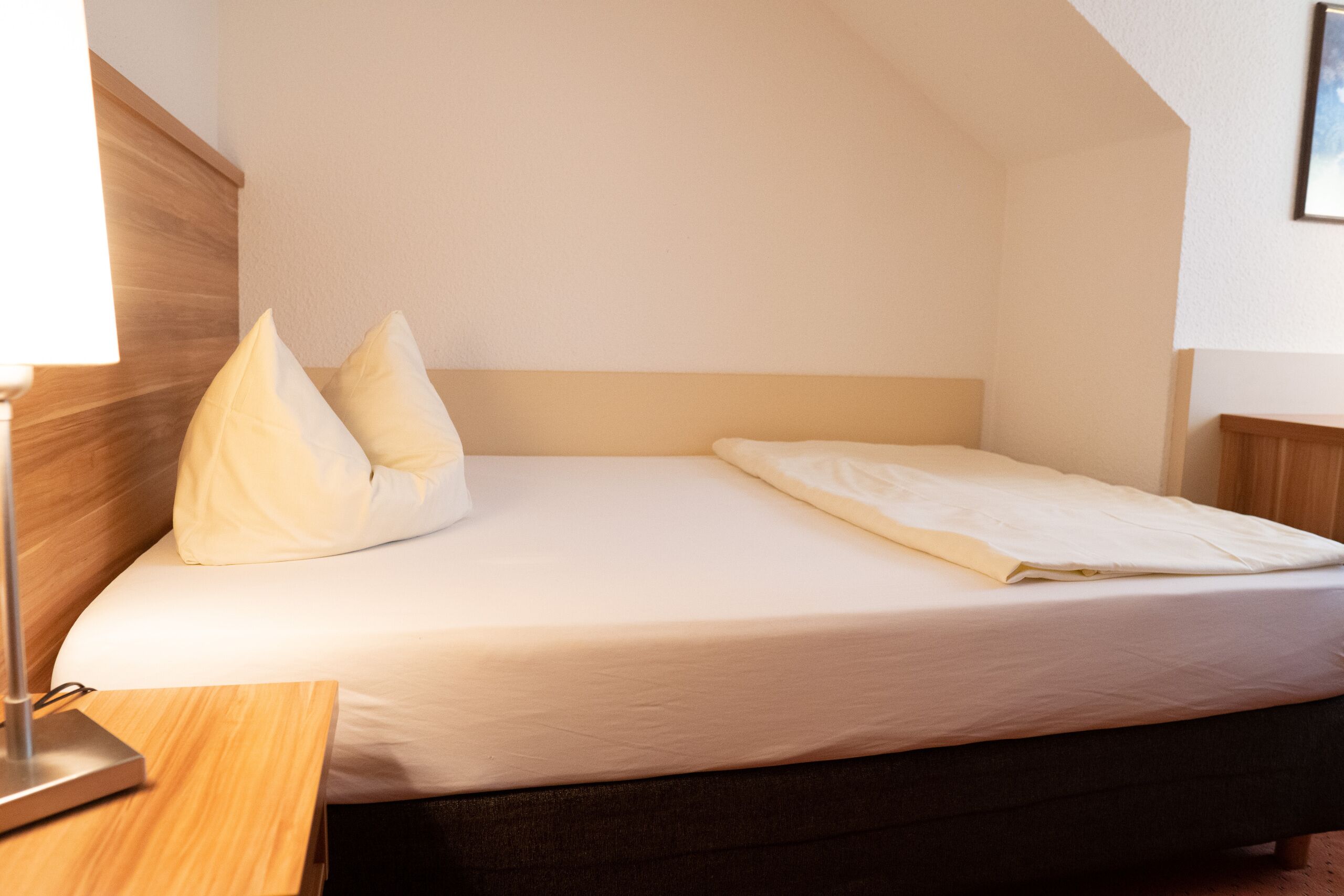 Una cama bien tendida con sábanas blancas en una habitación con cabecera y mesita de noche de madera.