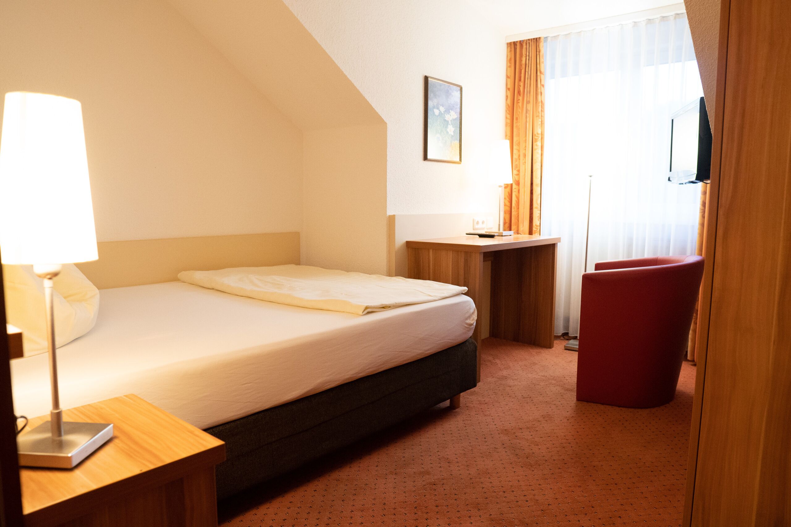 A hotel room with a bed, a desk, a chair, and a TV.