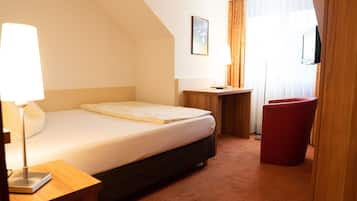 A hotel room with a bed, a desk, a chair, and a TV.