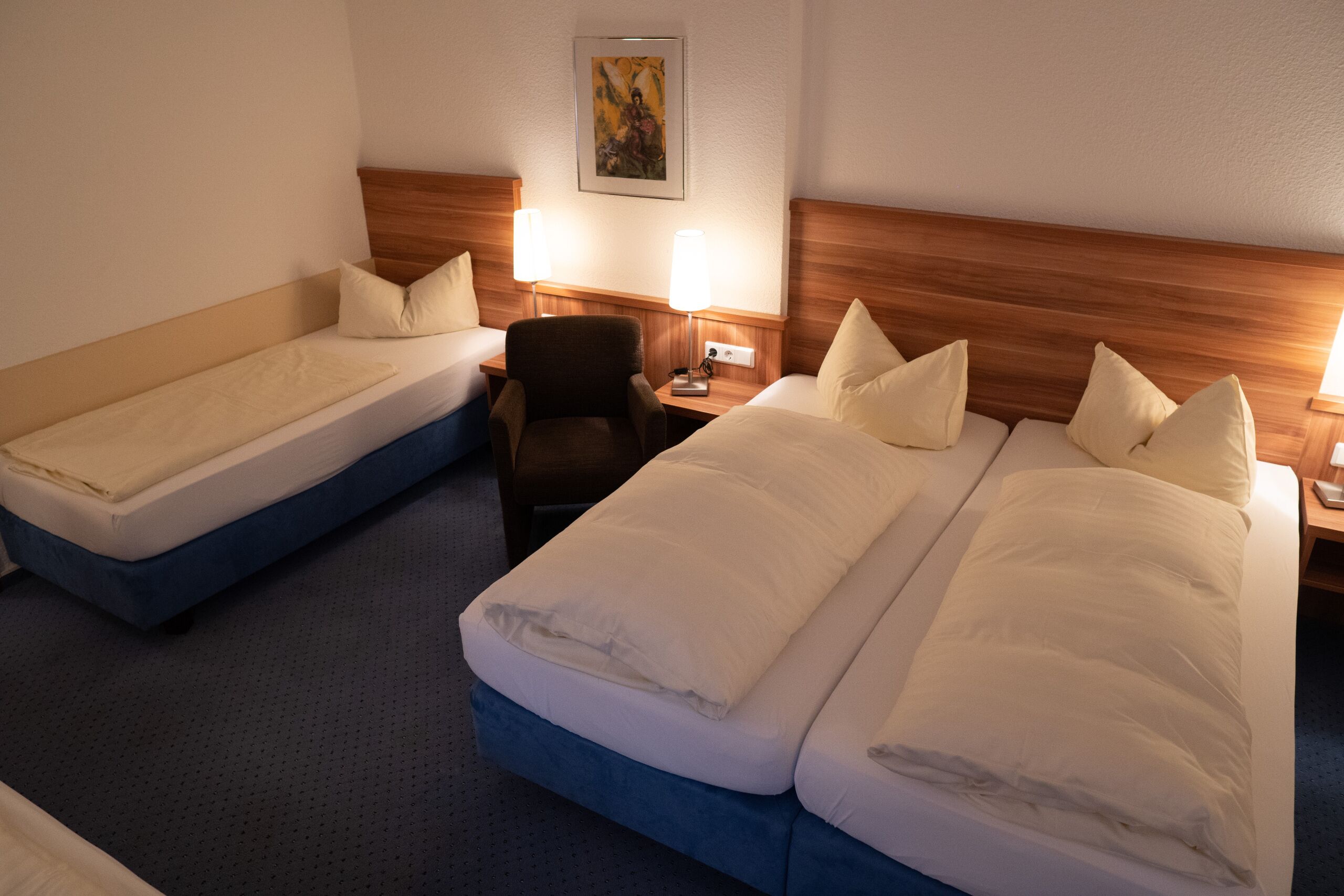 Ein Hotelzimmer mit zwei Einzelbetten, einem Holzkopfstück, einem Stuhl und einem Nachttisch mit einer Lampe.