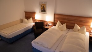 A hotel room with two single beds, a wooden headboard, a chair, and a nightstand with a lamp. - Hotel Jägerhof (Bad Hersfeld)
