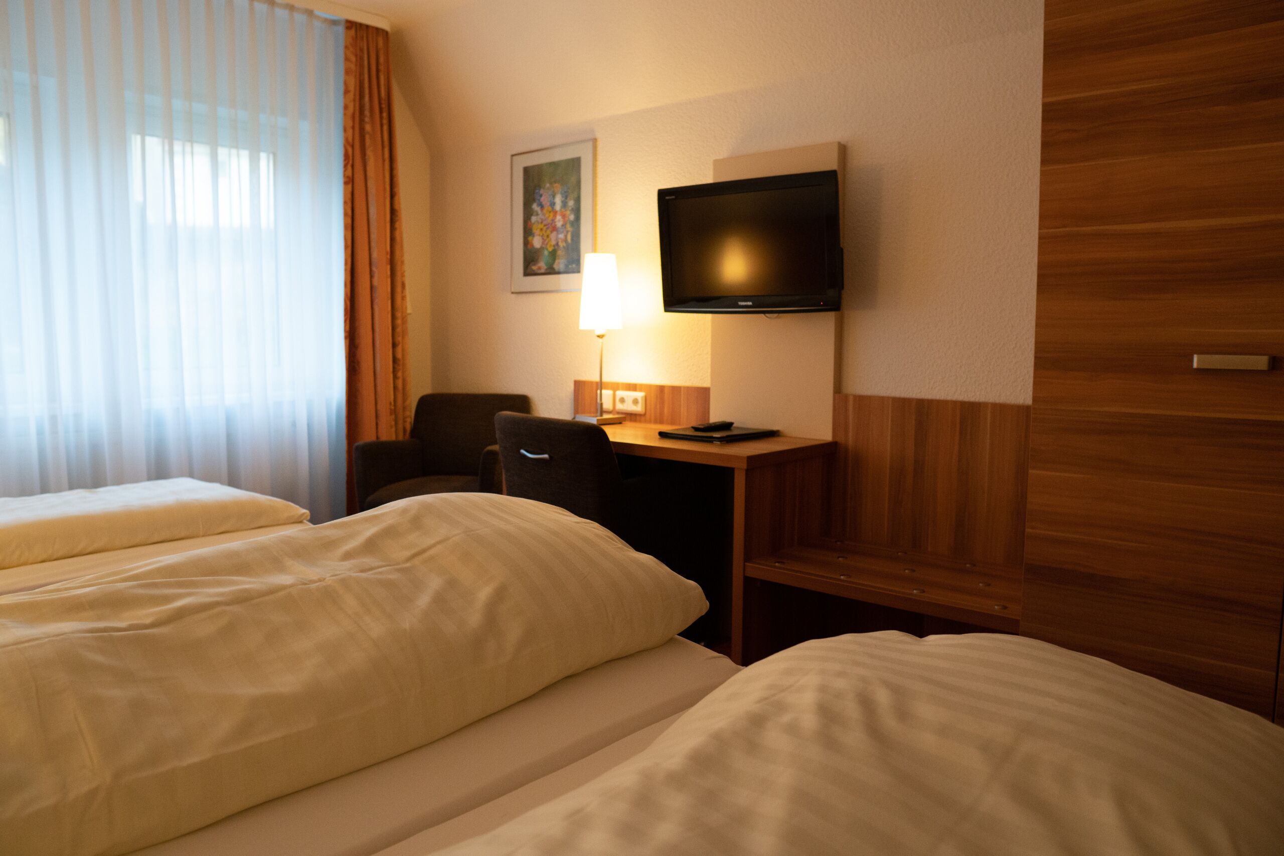 Ein Hotelzimmer mit zwei Betten, einem Schreibtisch, einem Sessel, einem Fernseher und einem Bild an der Wand.