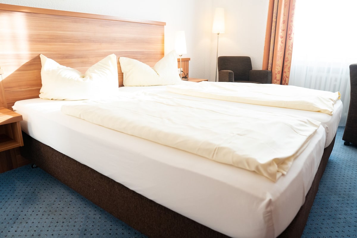Een hotelkamer met een groot bed, een houten hoofdeinde, een bureau, een stoel en een lamp.