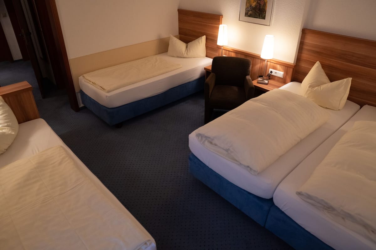 Een hotelkamer met twee eenpersoonsbedden, een stoel, een bureau met een lamp en een schilderij aan de muur.