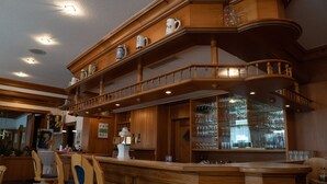 Un espace bar en bois à plusieurs niveaux, doté de sièges, d’un grand miroir et d’étagères où sont exposés des verres.