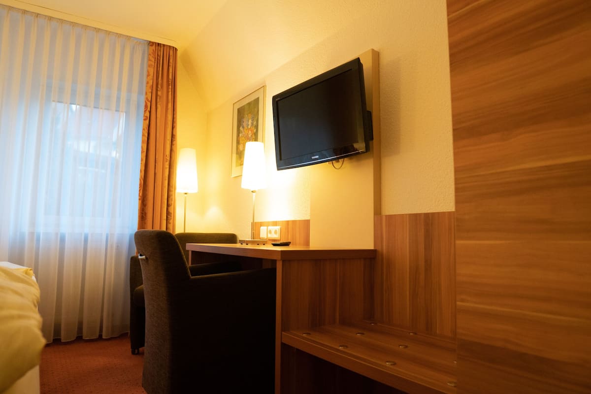 Hotelkamer met een bed, bureau, stoel, televisie aan de muur en een raam met gordijnen.