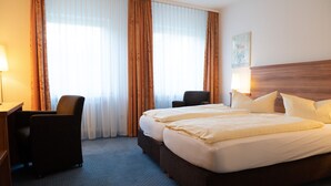 Une chambre d’hôtel avec un grand lit, deux chaises, un bureau et une lampe.