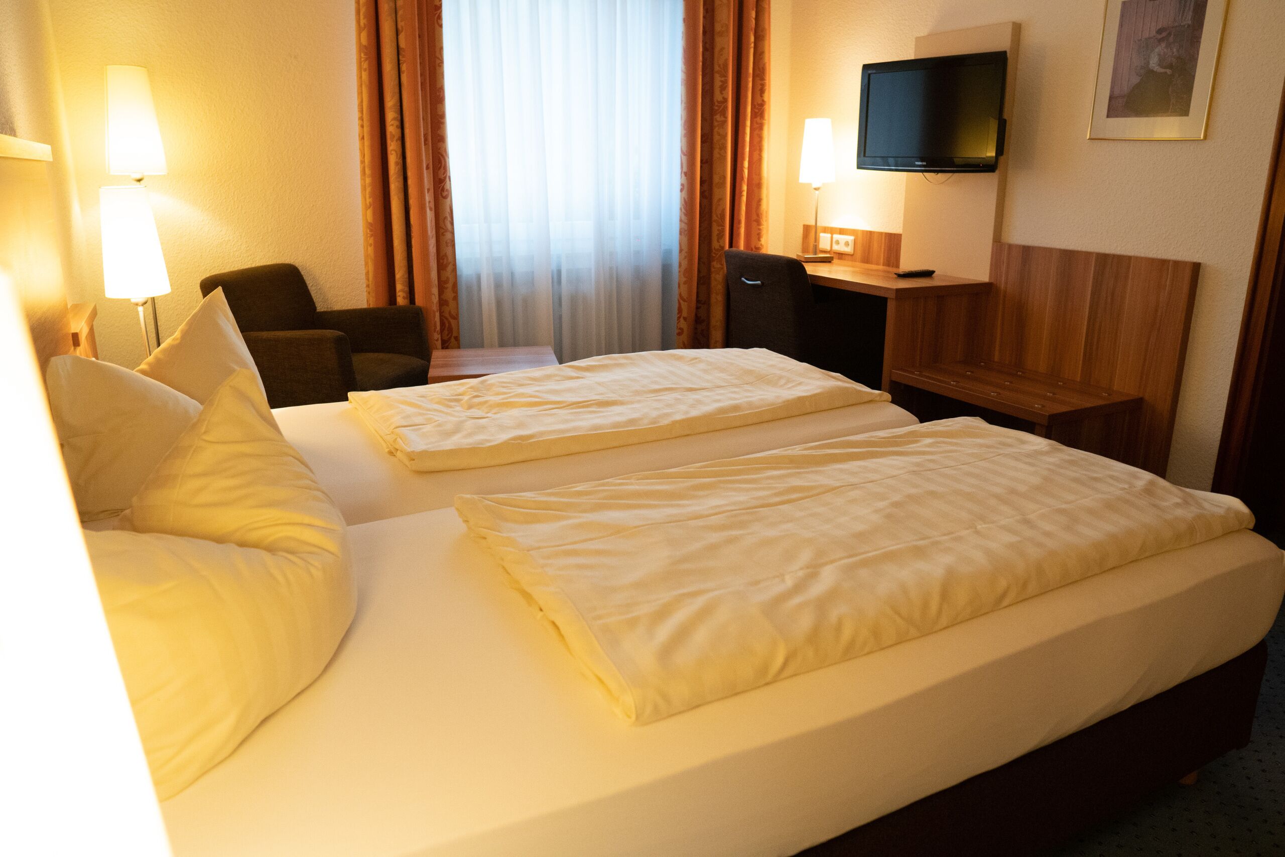 Una habitación de hotel con dos camas, un escritorio, una silla, un televisor y una lámpara.