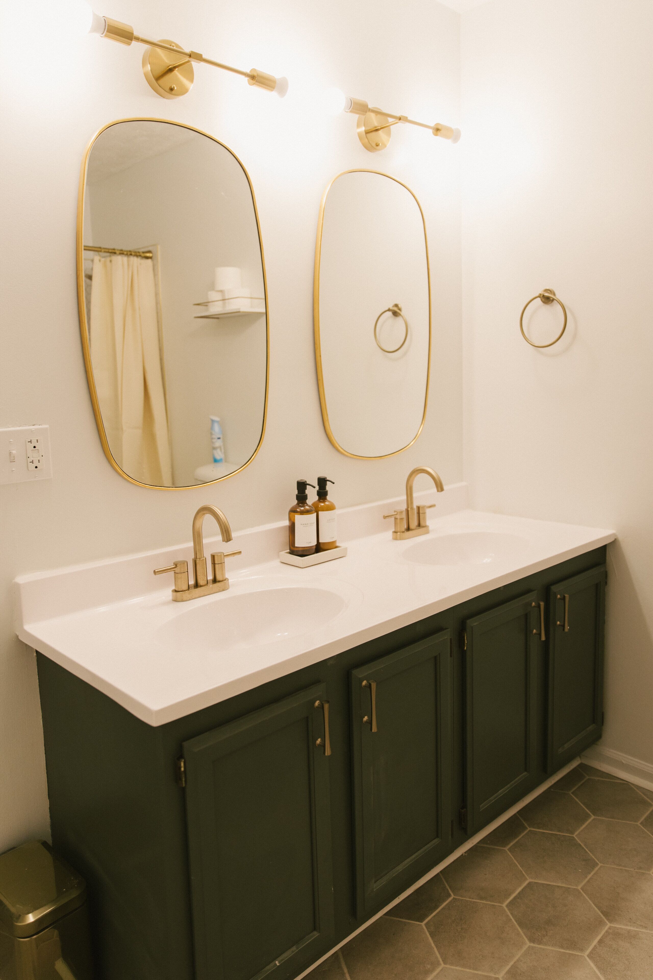 A bathroom with two sinks, gold fixtures, and green cabinets.