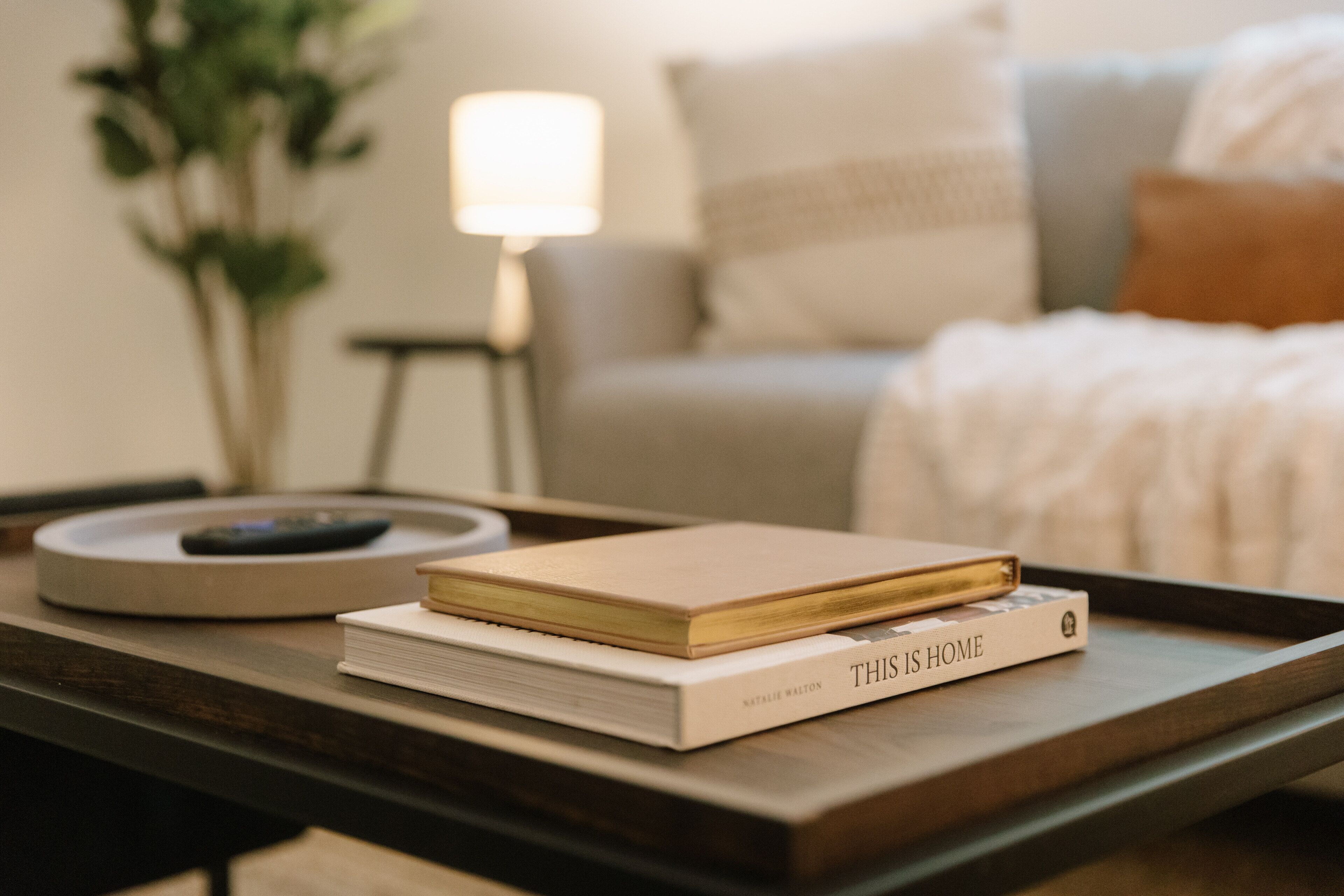 A book titled "THIS IS HOME" on a tray, with a lamp and a plant in the background.