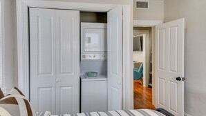 Un dormitorio con cama, un armario con lavadora y secadora, y una puerta que da a otra habitación.