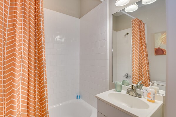 A bathroom with a white bathtub, a sink with toiletries, and a mirror reflecting the shower curtain.