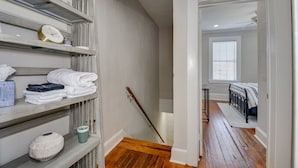 Una escalera conduce a un dormitorio con cama, mesita de noche y ventana con persianas.
