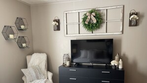 Un dormitorio con una cama, un televisor sobre una cómoda, una silla y adornos en la pared, incluyendo repisas hexagonales y una corona.
