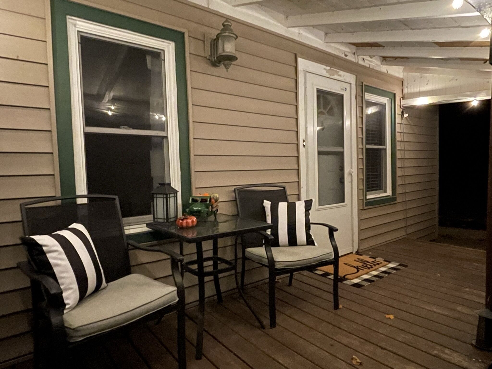 A covered porch with two chairs and a table, a lantern, and a pumpkin decoration.