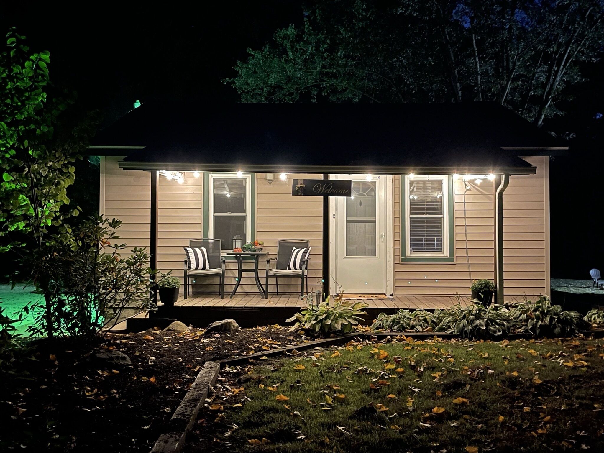 A small house with a porch, two chairs, and a table.