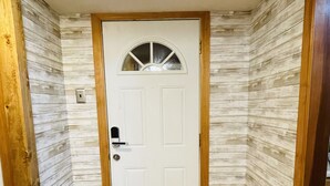 Un pasillo con piso de madera, una puerta blanca con un ventanal pequeño y paneles de madera en las paredes.
