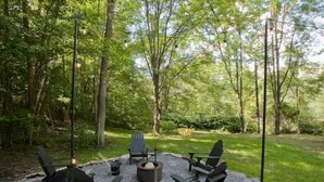 An outdoor seating area with four Adirondack chairs, a fire pit, and a small table.