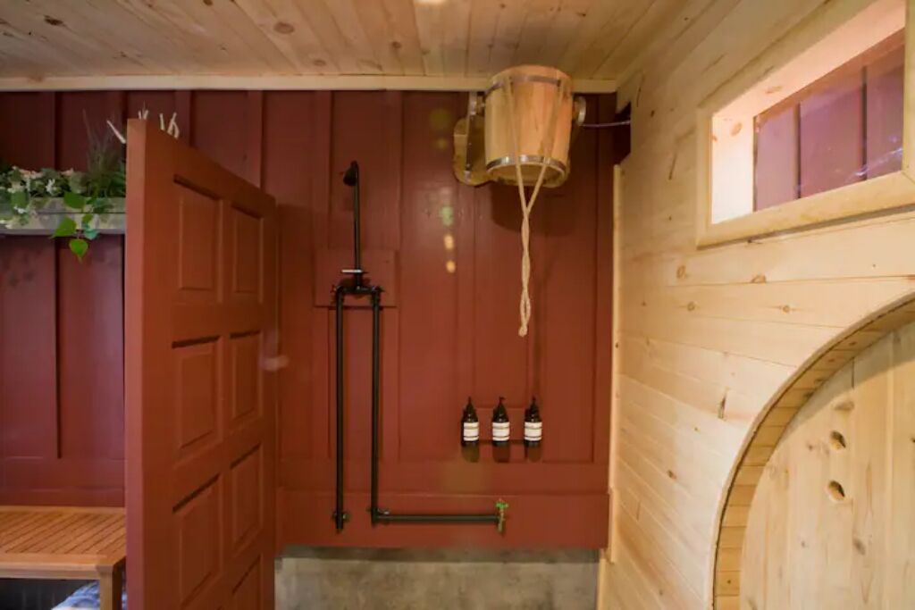 Ein Holzsaunaraum mit Holztür, einem hängenden Eimer und drei Flaschen an der Wand.