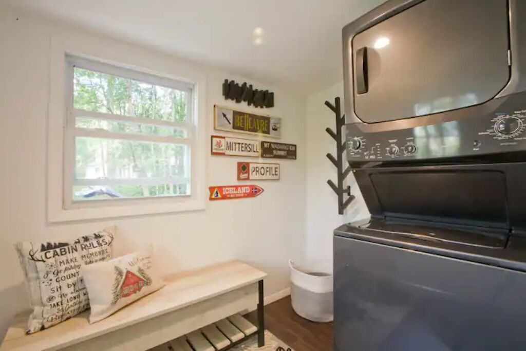 Een keuken met een ingebouwde oven, een raam met uitzicht op bomen en wanddecoraties, waaronder borden en een kussen met tekst.