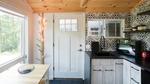A compact kitchen with a white door, wooden ceiling, and patterned backsplash.