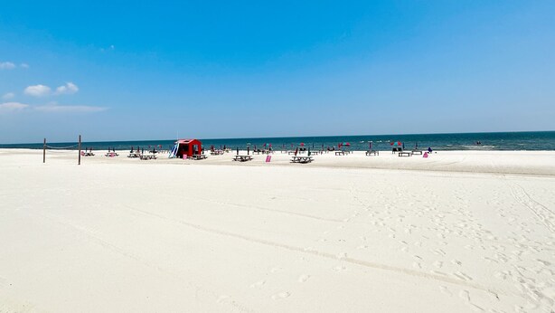 A wide sandy beach with picnic tables and a red lifeguard station. - BeachView-Arcade-Walk to Beach-Restaurants-Casino (Gulfport)