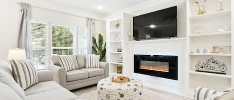 A modern living room with a fireplace, comfortable seating, and a flat-screen TV.