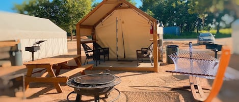 A camping site with a tent, picnic table, chairs, and a fire pit.
