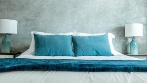 A neatly made bed with blue pillows and a blue throw blanket, two bedside tables with lamps, and a textured gray wall. - Private Guest House  -Villa in the Valley- (Nanaimo)