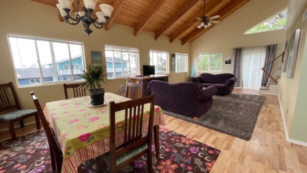 Une pièce spacieuse avec un plafond en bois, une table à manger avec des chaises, un canapé violet et un téléviseur.