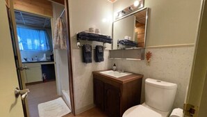 Ein kleines Badezimmer mit Toilette, Waschbecken und Spiegel. Ein kleines Fenster mit Vorhang und Holzboden.