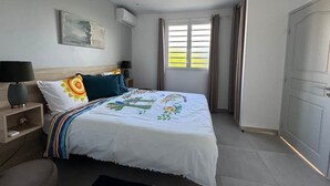 Ein Schlafzimmer mit Bett, Nachttischen, einem Sessel und einem Fenster mit Vorhängen sowie einer Tür.