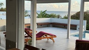 Ein überdachter Außenbereich mit Pool, Liegestühlen und Meerblick.