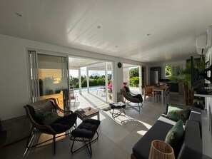 Un vaste espace de vie comprenant une porte-fenêtre coulissante donnant sur un balcon, un canapé, une table basse et un coin repas avec des chaises.