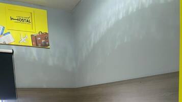 Una habitación pequeña con cama individual, cabecera de madera, colcha amarilla, una mesita y una silla.