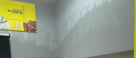 Una habitación pequeña con cama individual, cabecera de madera, colcha amarilla, una mesita y una silla.