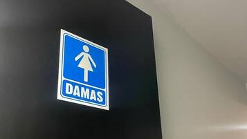 Ein blaues Schild mit einer weißen Frauenfigur und dem Wort 'DAMAS' an einer schwarzen Wand.