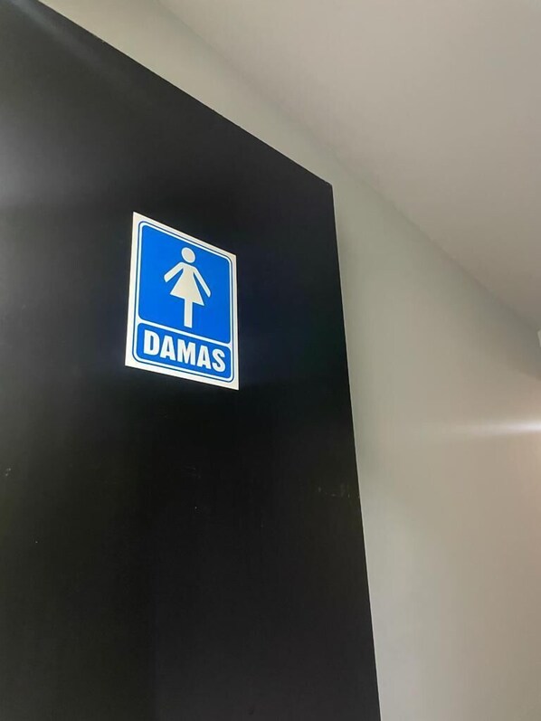 Un letrero azul con la silueta de una mujer y la palabra 'DAMAS' sobre una pared oscura.