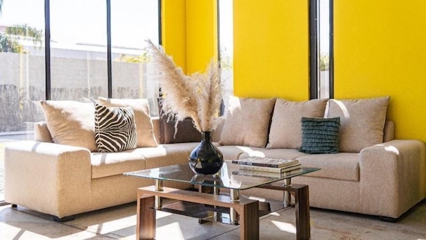 Una sala de estar moderna con un sofá color beige, una mesa de centro de vidrio y un jarrón con plantas secas.
