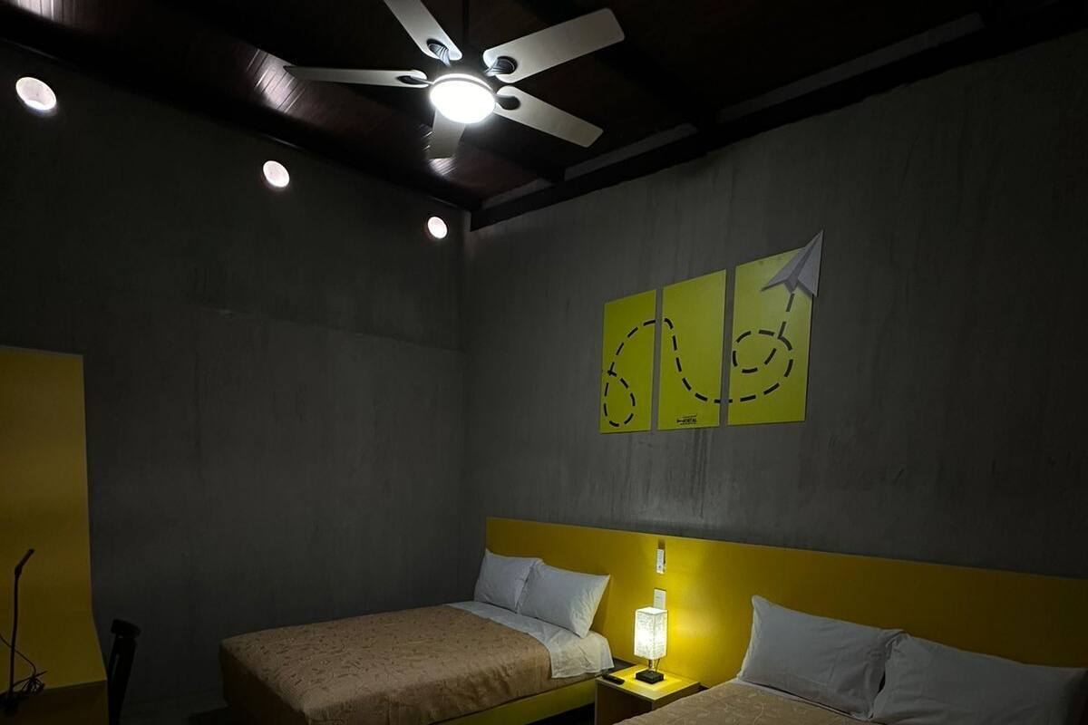 Une chambre d’hôtel avec deux lits, un ventilateur de plafond et des œuvres d’art murales.