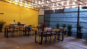 Un comedor interior con paredes amarillas, varias mesas y sillas, y plantas en macetas.