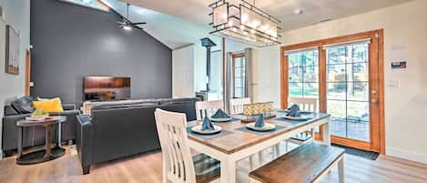 Una sala moderna con pared gris oscuro, un sofá de cuero negro, una mesa de comedor de madera y sillas blancas, y un ventilador de techo.