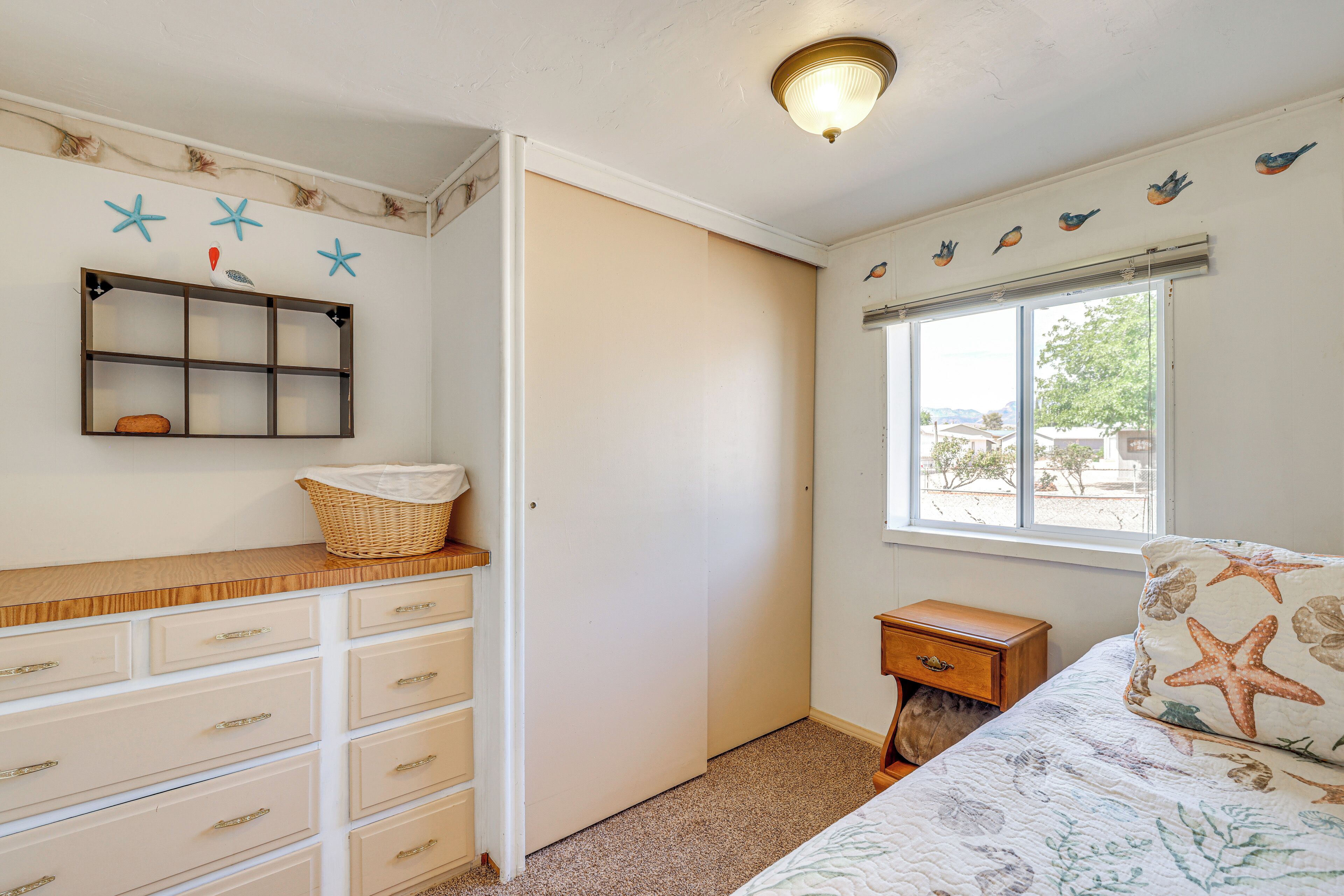 A bedroom with a bed, dresser, window, and wall decorations.
