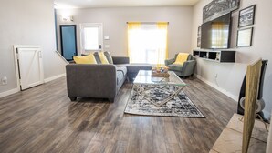 Ein modernes Wohnzimmer mit einer Couch, Sesseln, einem Couchtisch und einem Fernseher.