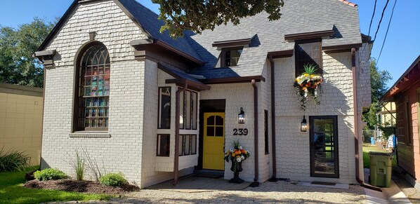 A two-story house with a yellow door, numbered 239, and a large arched window. - Quirky historic home, fully renovated! Designer interior! Plush linens! Firepit! (New Iberia)