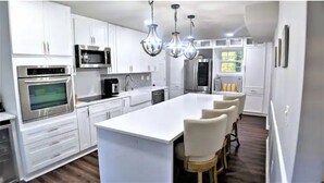 A modern kitchen with white cabinetry, stainless steel appliances, and a central island with bar stools. - The Red Magnolia, Refreshing, Cozy, Game Room, Historic Roswell! (Roswell)